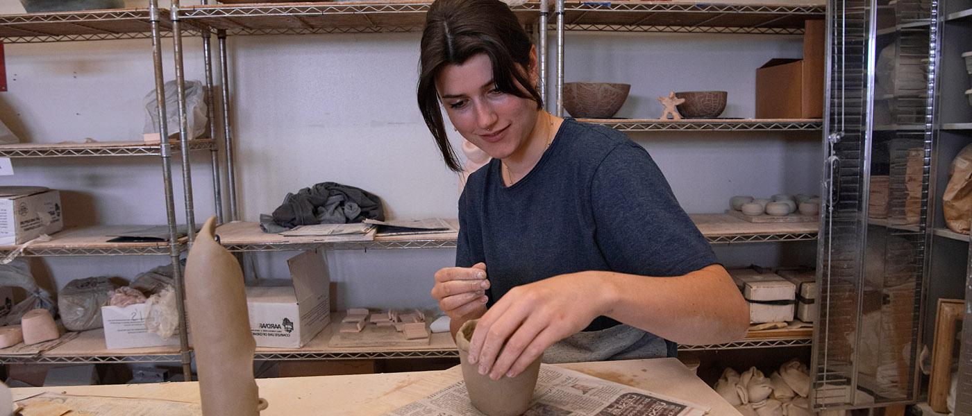 微笑的艺术学生看着镜头，她用釉画一个陶瓷项目